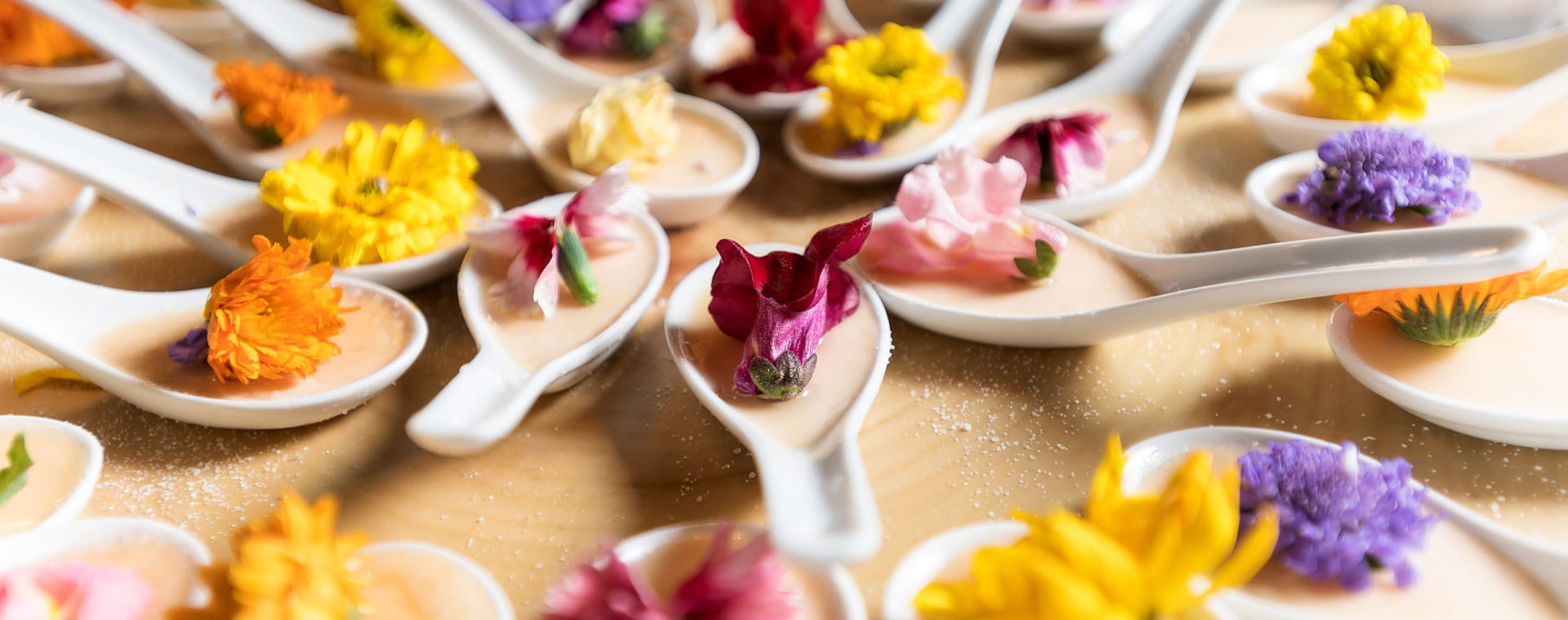 White ceramic soup spoons filled with custard and an edible flower on top
