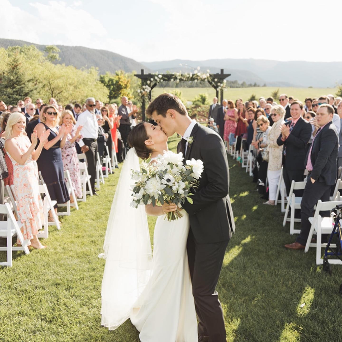 A bride and groom kissing down the aisle at their wedding ceremony that is outside