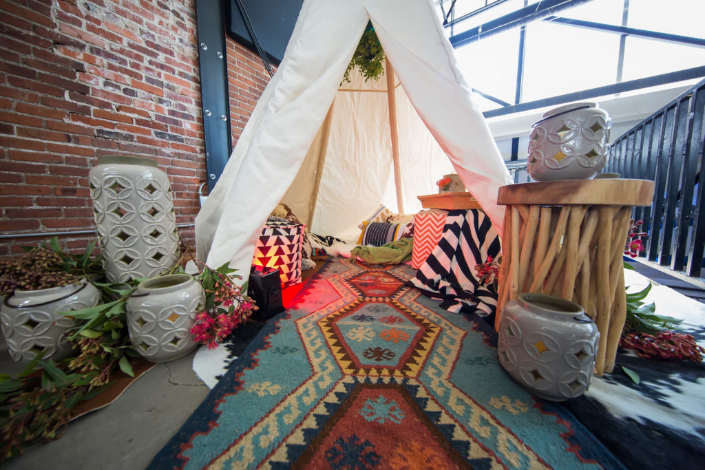 A small white indoor tent with a colorful long runner and different patterned pillows and square ottomans