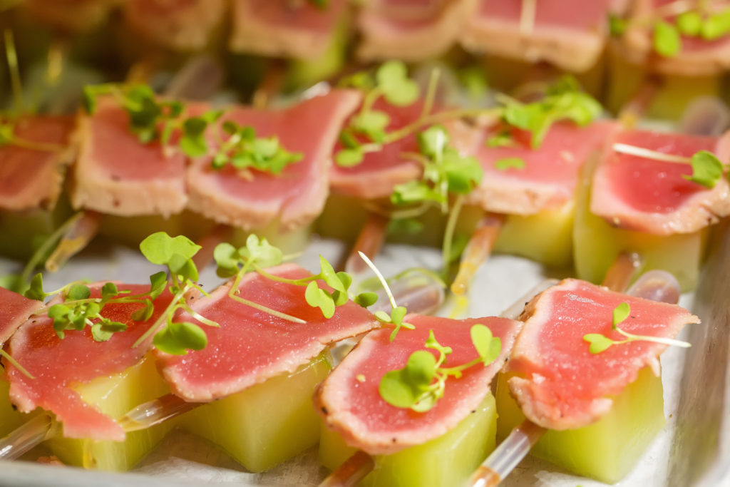 thin pieces of seared tuna sitting on a piece of melon with a pipette full of liquid and microgreens on top
