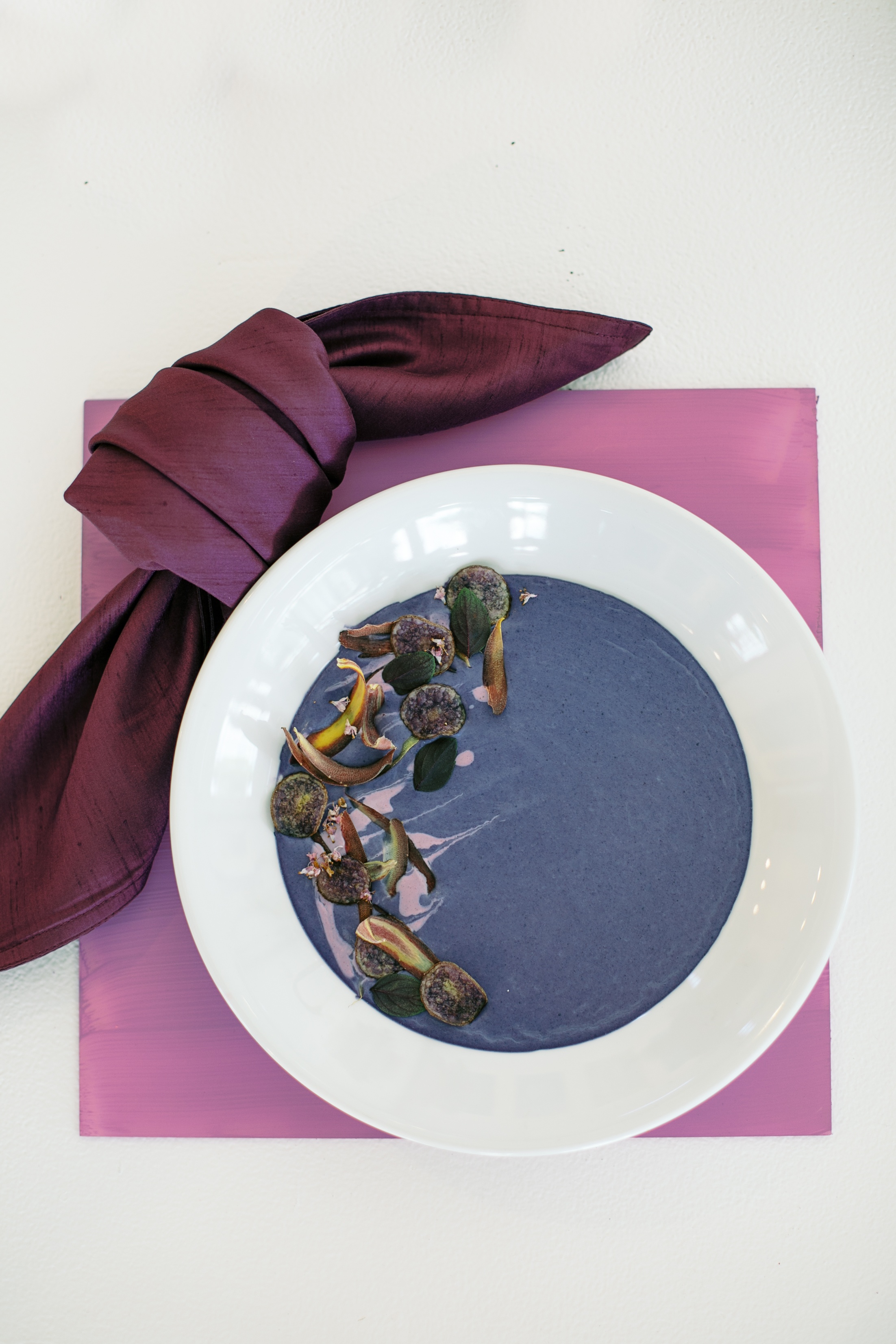 purple potato soup on a purple placemat with a purple napkin in a knot in the upper left corner in front of the bowl of soup