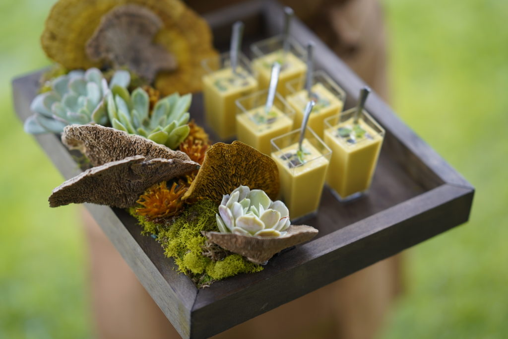 6 small soups in tall rectangles on a wooden tray with moss, succulents and flowers