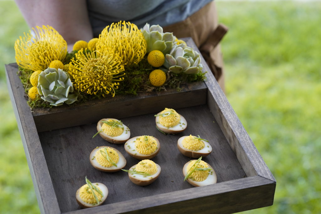 beet Deviled eggs on a wooden tray with moss, succulents and flowers