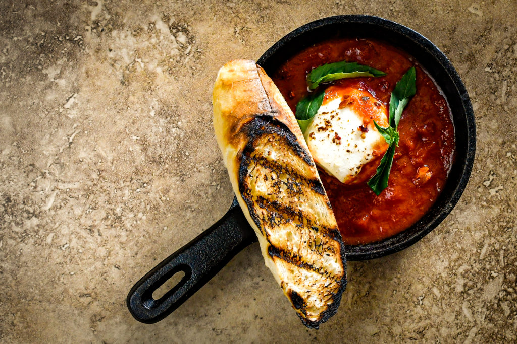 queso de cabra in a mini skillet with fresh herbs and a piece of grilled bread on top