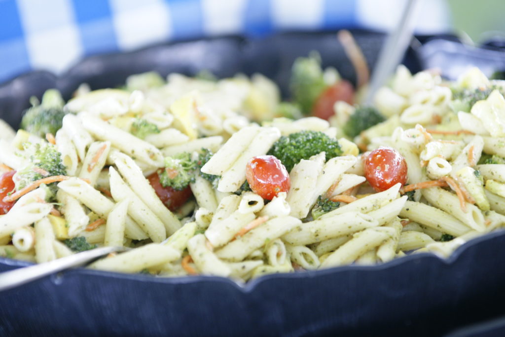 close up of vegetable penne pasta salad with broccoli, cherry tomatoes and shredded carrots