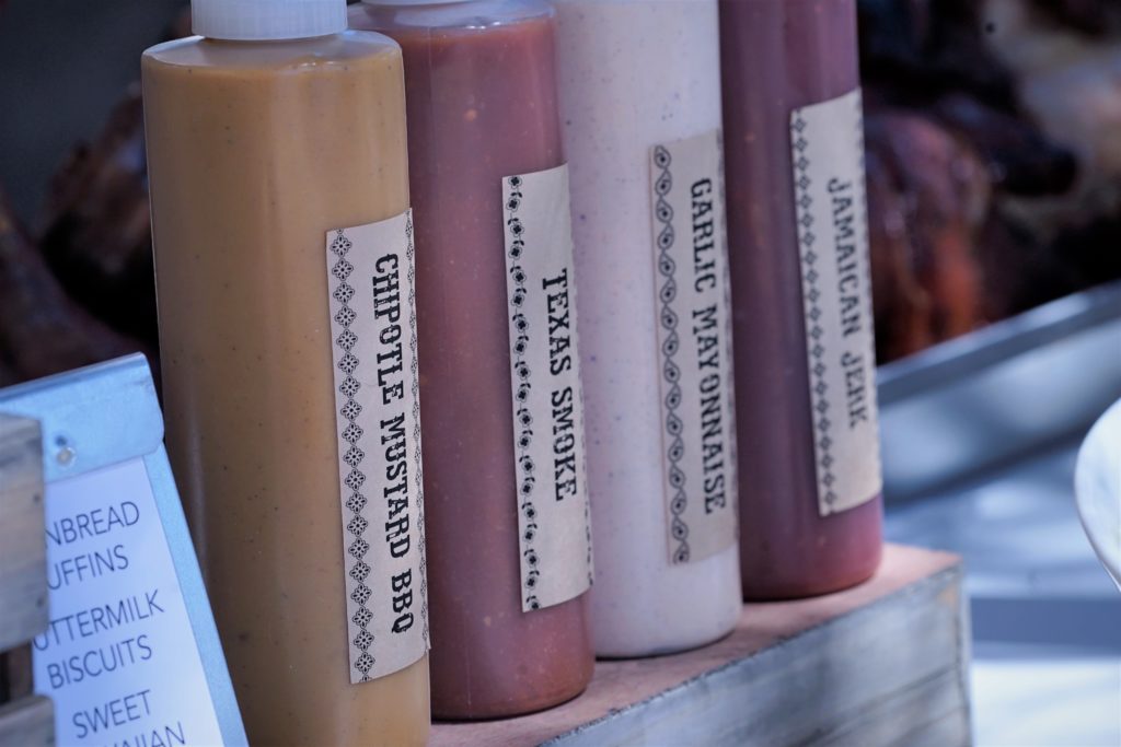 close of four plastic bottles each with a different bbq sauce labeled from left to right as "chipotle mustard bbq", "texas smoke", "garlic mayonnaise" "jamaican jerk'