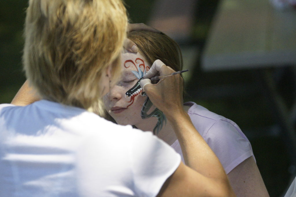 A women is face painting a dragon onto a young girls face