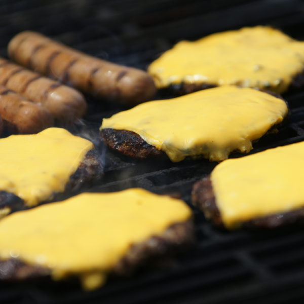 five cheeseburgers and four hot dogs on the grill