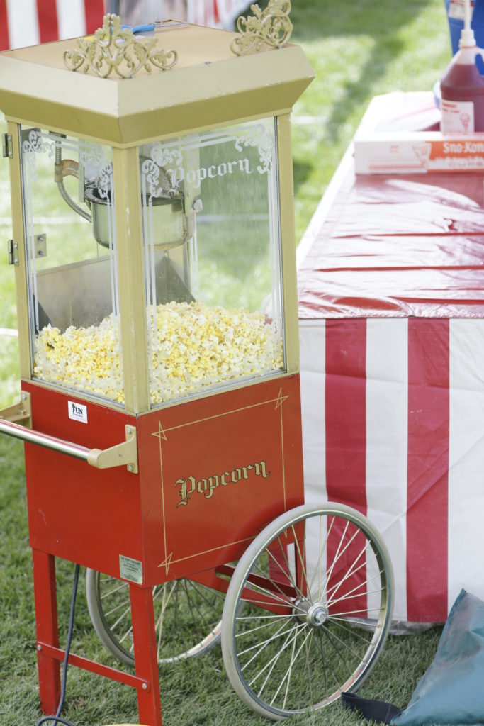 A red popcorn machine outside at a picnic popping popcorn