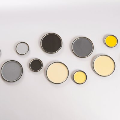 Different sizes and shades of grey and yellow paint lids on a white background