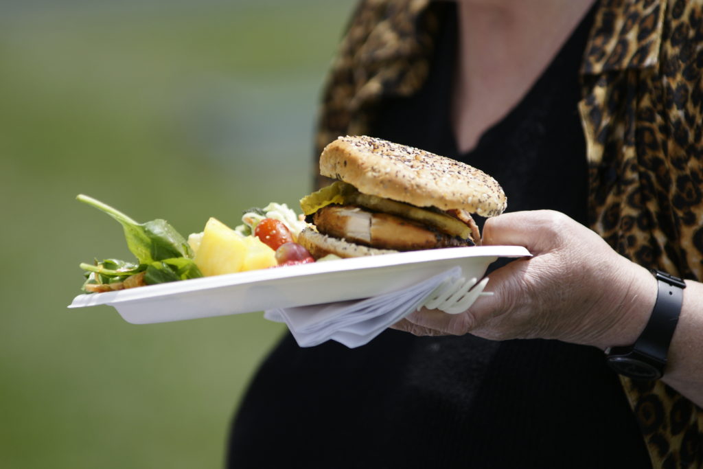 A plate with some sort of burger, fresh fruit and salad being carried by a women in black with an unbuttoned cheetah print jacket shirt