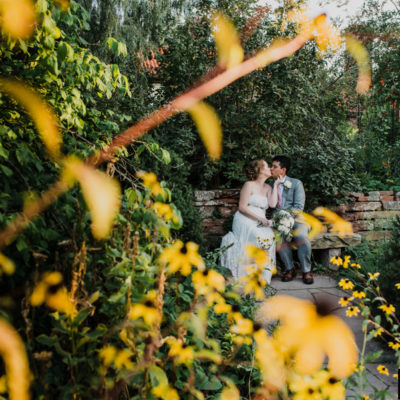 A bride and groom sharing a kissing on a stone bench in a garden