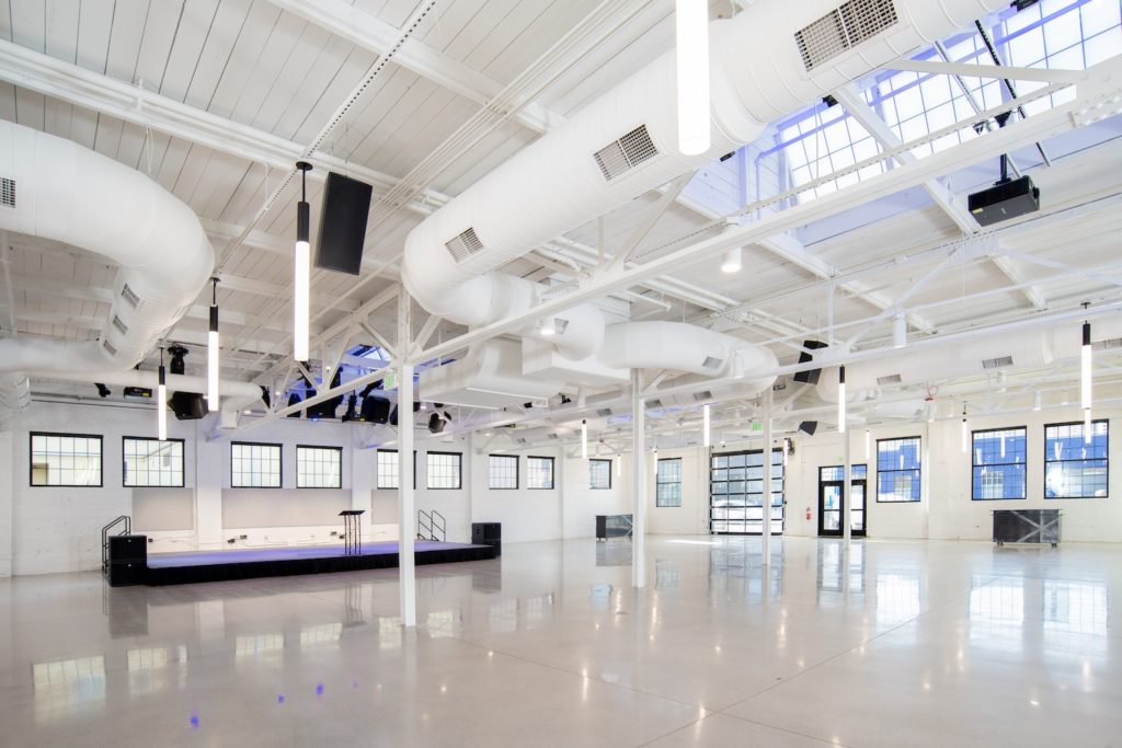 A large open venue with white walls, a shiny white tile floor, white ceiling and white pipes giving the vneue a modern industrial feel