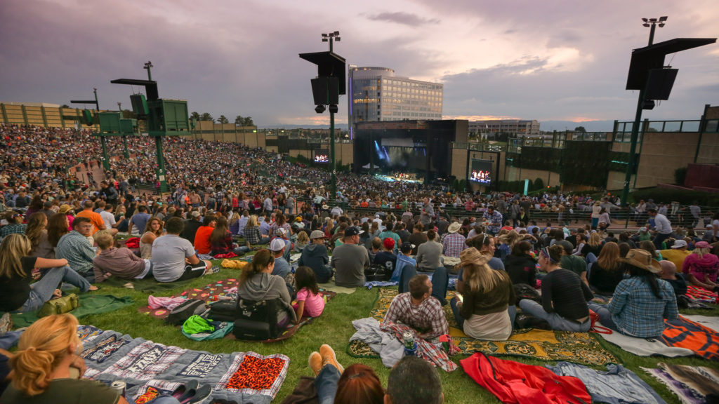 A large group of people sitting outside at Fiddler's Green ampitheatre enjoying a concert