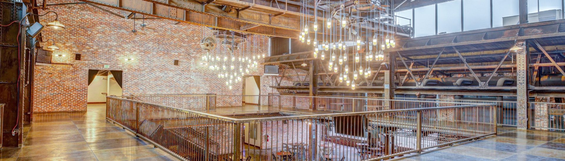 An open second floor with industrial ceiling, large tiled floor, red brick walls and 2 large chandeliers made with lots of light bulbs. The middle overlooks to the first floor.