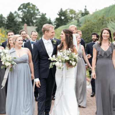 A bride, groom and wedding party outside walking down a brick path