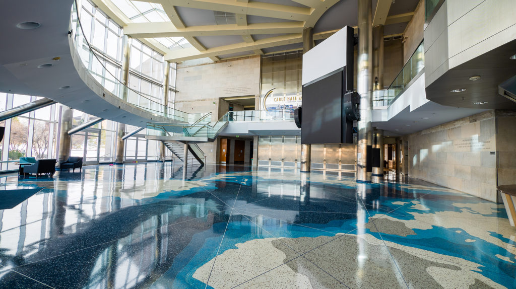 A large open venue with a tile floor made to look like a map with large open windows to the left and a second floor that is open to the first floor
