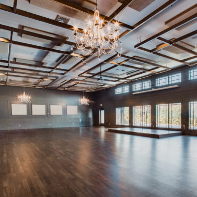 Inside a ballroom with beautiful brown plank flours, and a raised stage in the back.
