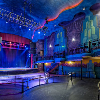 A large open theatre with no people around. The walls are painted colorfully. Blue and red lights are on to create a moody feeling.