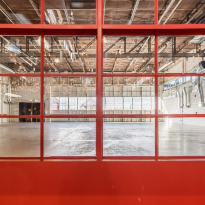 A large red window looking into an empty industrial room with lots of hanging lights from the cieling