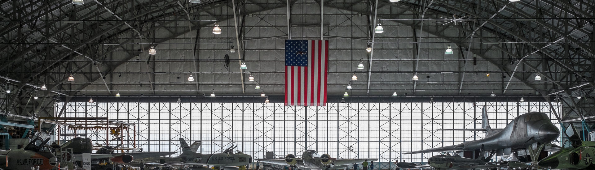 Airplane hanger full of airplanes and a large American flag hanging down from the ceiling in the center