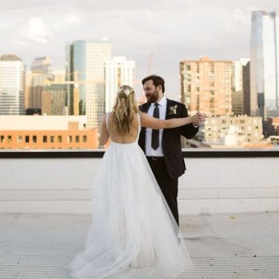 A bride and groom dancing on a rooftop with the city of denver in the background