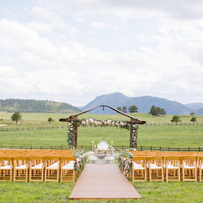 A wedding ceremony with light brown chairs set up outside at spruce mountain ranch overlooking the ranch and the mountains in the far distance.