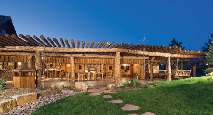 The outside of Spruce Mountain Ranch's patio which has wooden tables and wooden chairs. In the front, is freshly cut grass with a stone path leading to the patio.