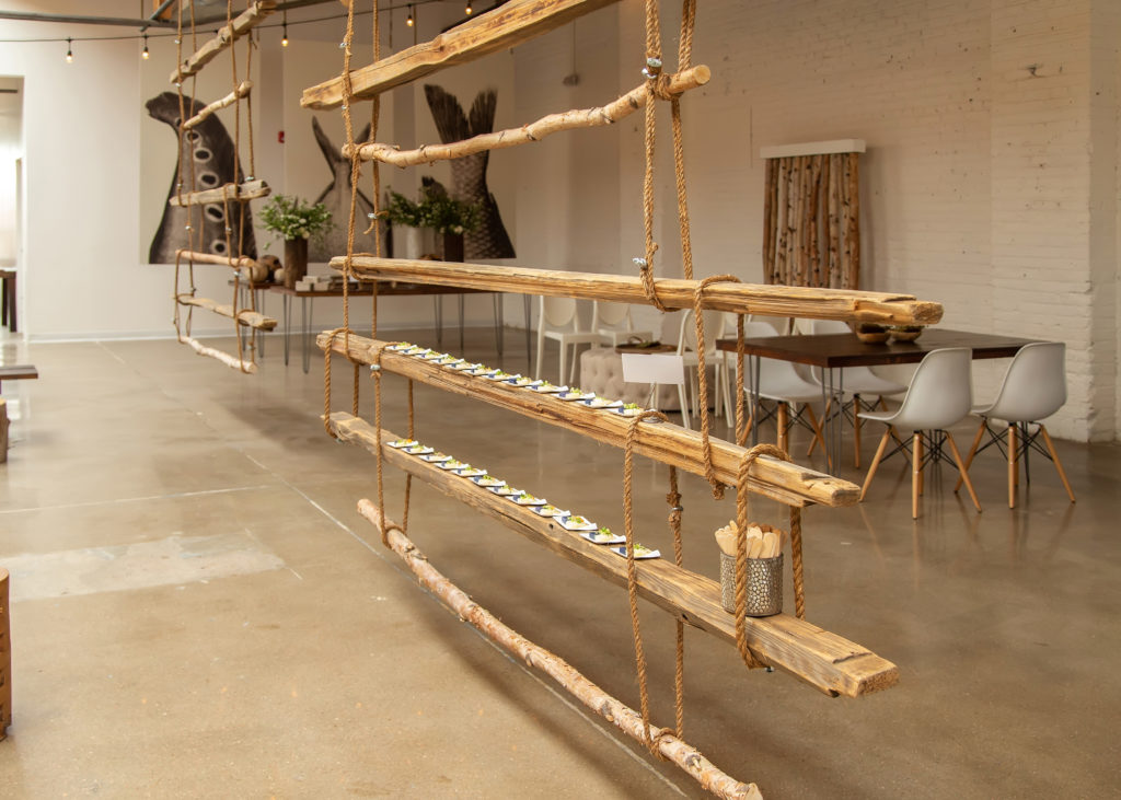 Thin wooden planks tied together with thick rope to form a long display with mini square on the beam with carrots & potato dishes.