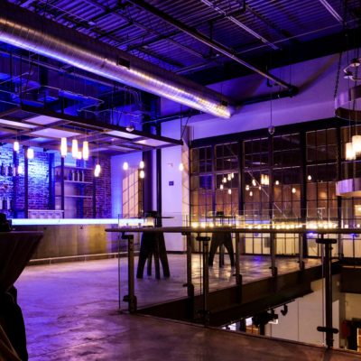 The second floor at Archetype Distillery showing the bar under neon blue and purple lights