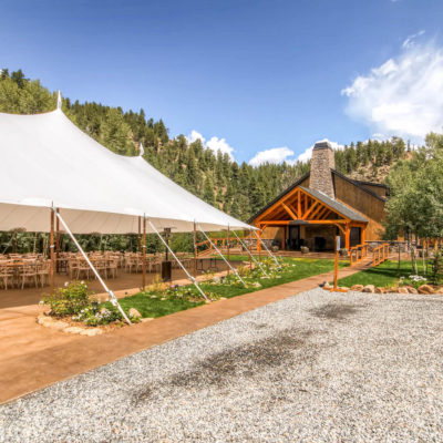 Outside of Blackstone Rivers Ranch Grounds 13, a large white text is in from of the building with wooden round tables and wood chairs set up for a reception