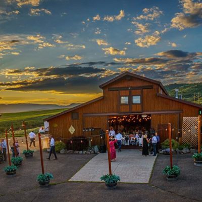 A wedding at La Joya Dulce with the sun setting and rolling hills in the background. Some guests are wandering outside to enjoy drinks.