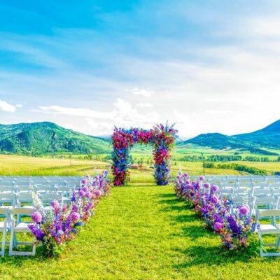 A wedding ceremony set up with white chairs with mountains in the background and lots of florals
