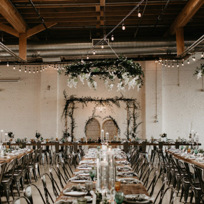 Indoor Skylight Venue set up for a wedding reception with rustic wooden tables, dark metal chairs, small hanging lights and lots of white flowers and greenery