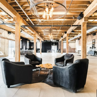 Indoor at Shyft at Mile High showing the wooden roof structure, industrial lambs and black leather chairs with a black rug and wooden table.