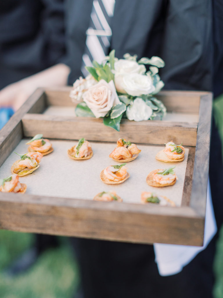 Passed hors d'oeuvre with shrimp on a wooden tray with a small floral rose arrangement to the side