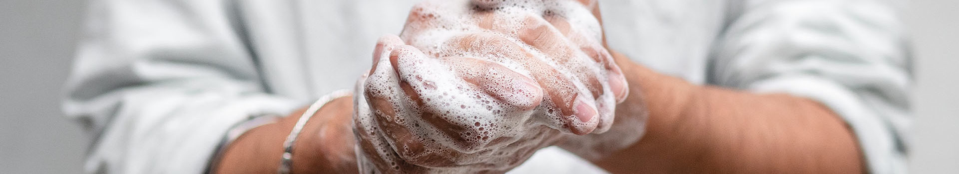 Close up of a person in a white button down shirt washing their hands with lots of soap.