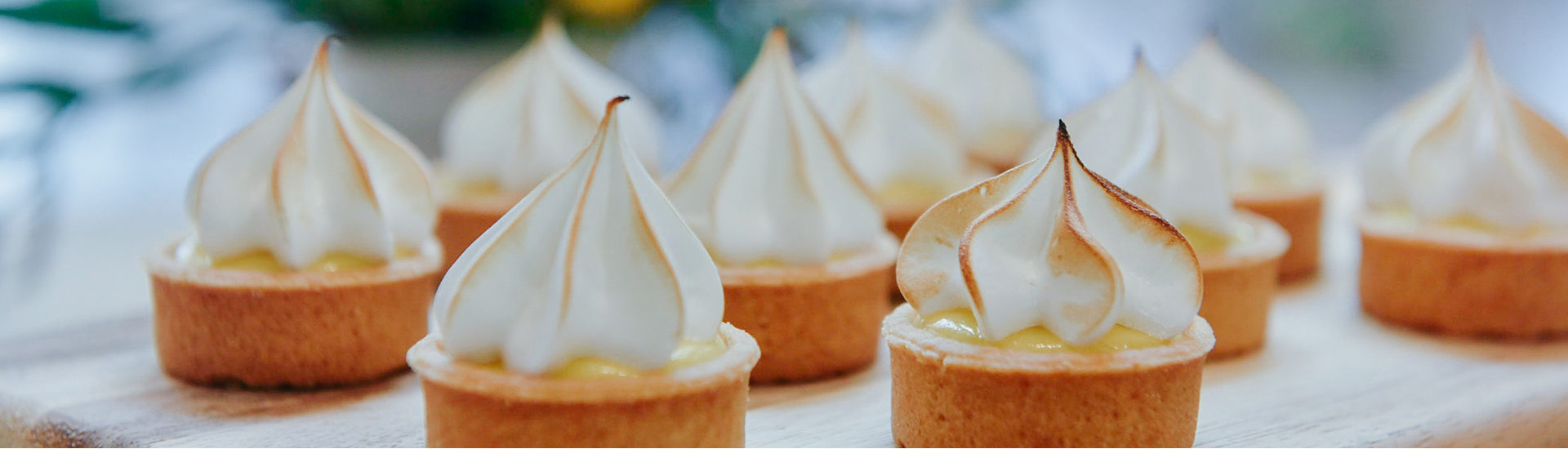 multiple mini lemon meringue tarts on a wooden board