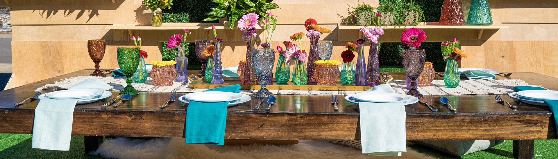 Large wooden table decorated with colorful vases full of different colored pink flowers and plated with different shaded of blue napkins