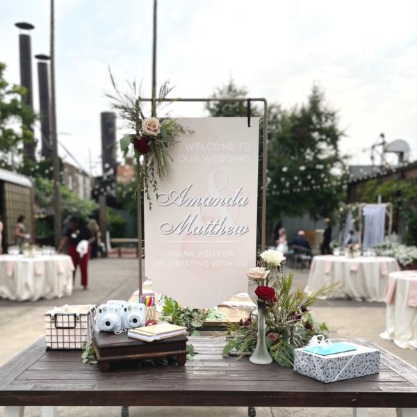 Pink welcome wedding right on a wooden table with flowers, surrounded by trinkets