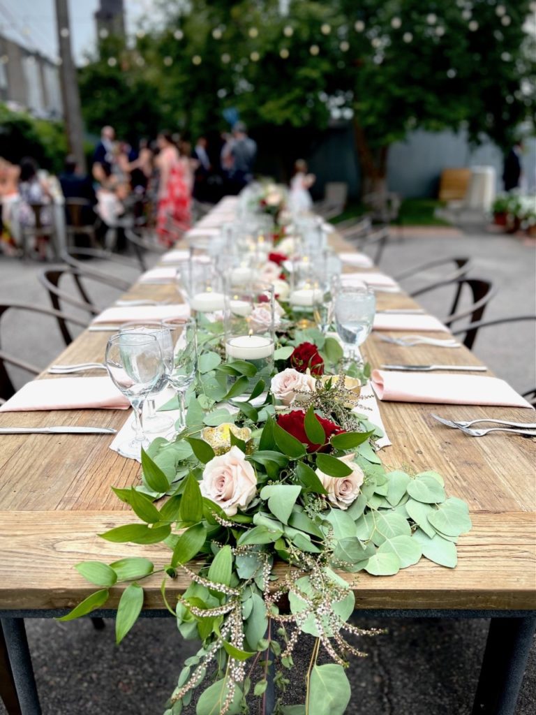 Wooden table with metal table surrounding with a garland runner with lots of greenery and pink and red roses