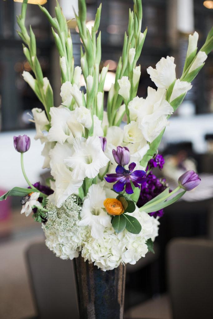 A tall floral arrangement with mainly white flowers, a few purple and orange accent florels
