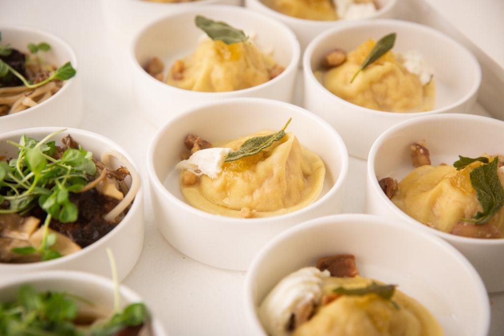 Multiple small circle bowls with a ravioli with a leaf of sage, nuts and a bit of burrata