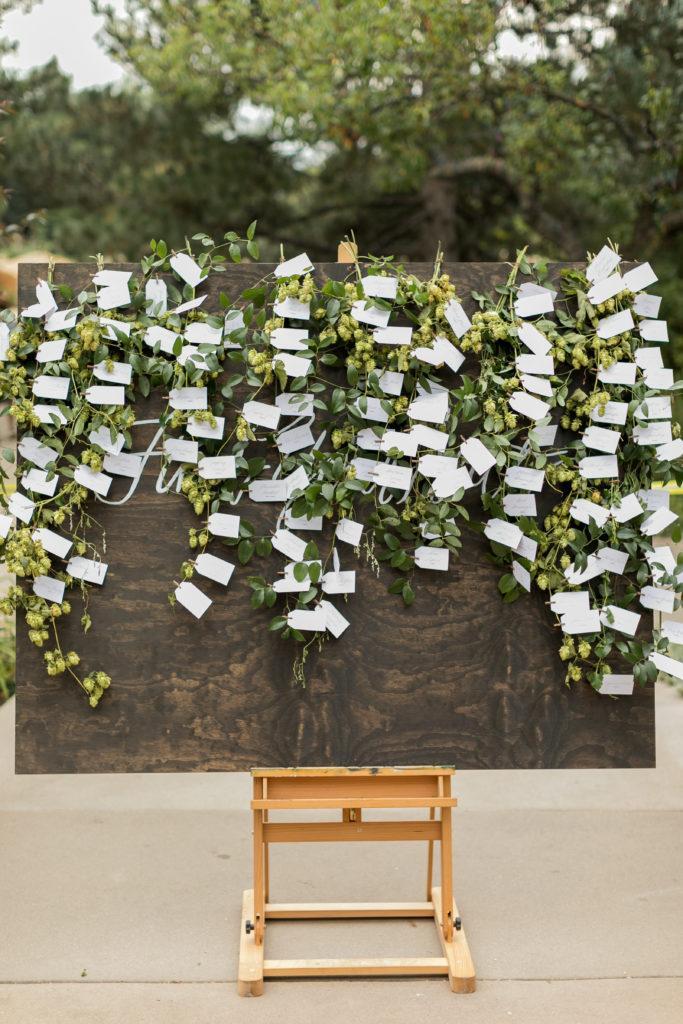 A large rectangle dark wood with lots of greenery that have white tags attached with clips on a wooden easel