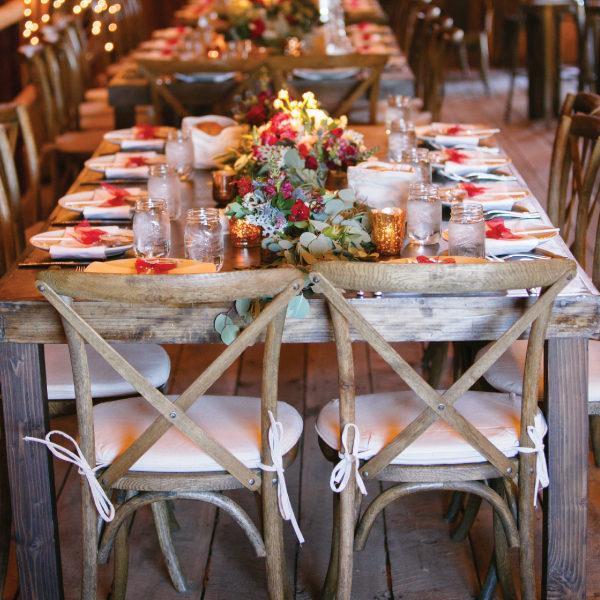 A wooden table with wooden chairs in the center are flowers and votive candles with water in mason jars