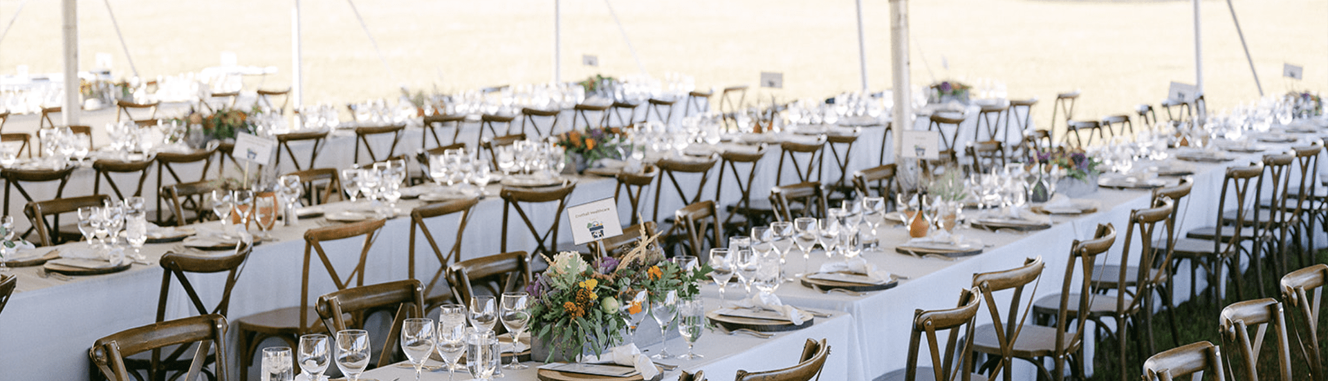 long rectangle tables under a white tent set up for a reception