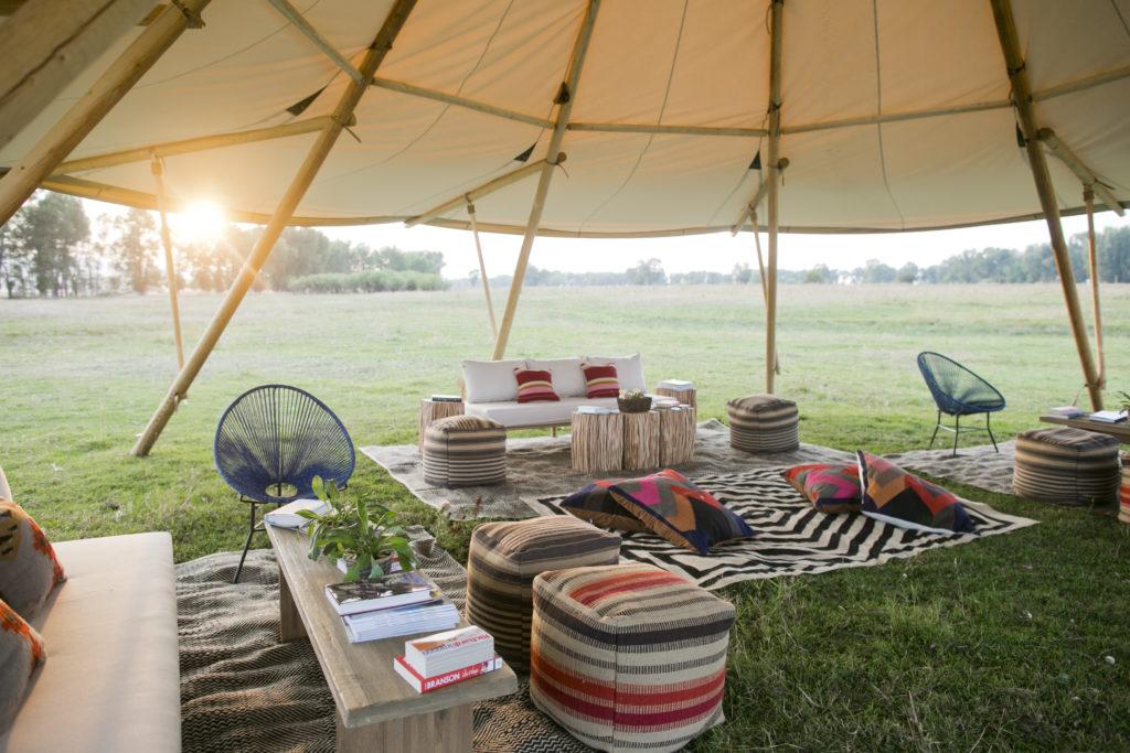 Boho lounges are under a large tent in a field with the sun in the background