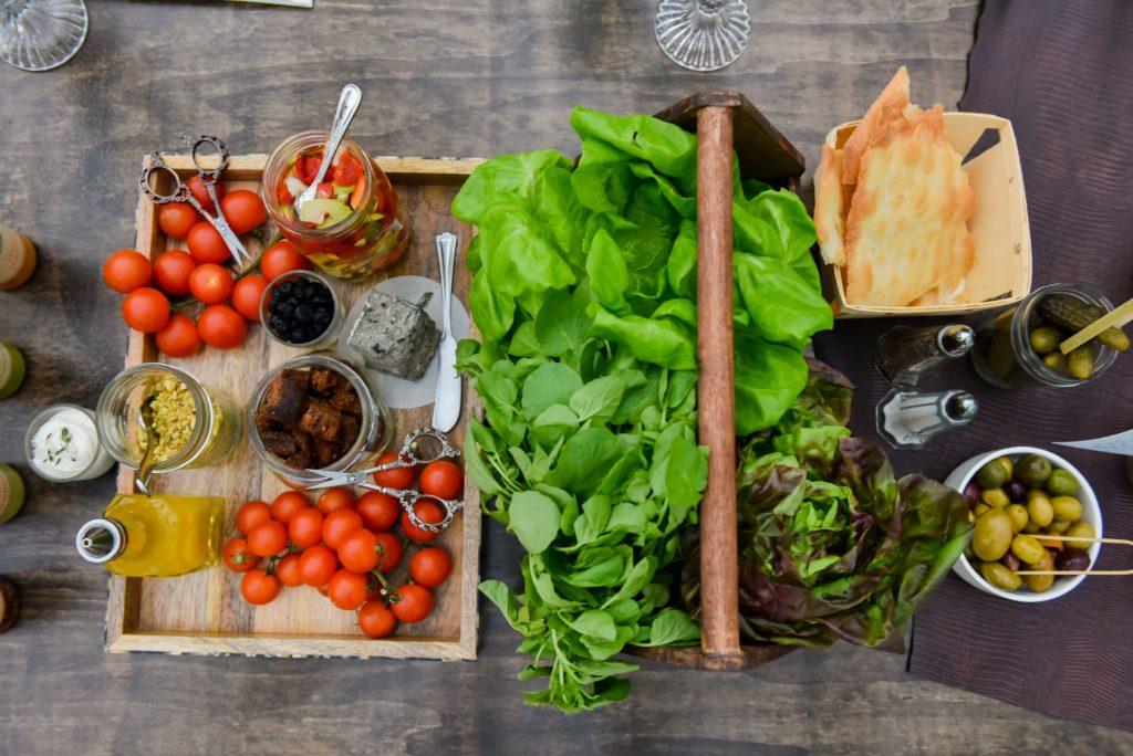 Overhead of living salad with lettuce in one box and a wooden tray with tomatoes, dressing, etc. 