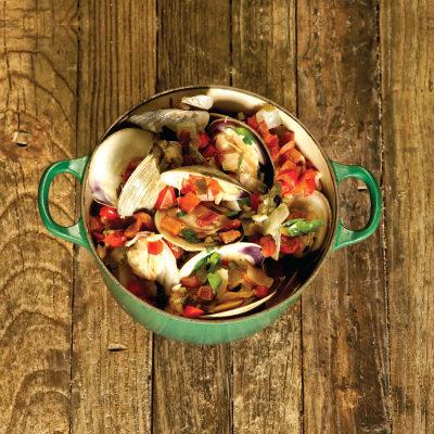 Little neck clams with tomatoes in a green dutch oven on a brown wooden background