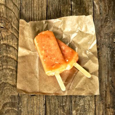 2 Peach popsicles stacked on top of each other of a piece of brown kraft paper on a wooden background